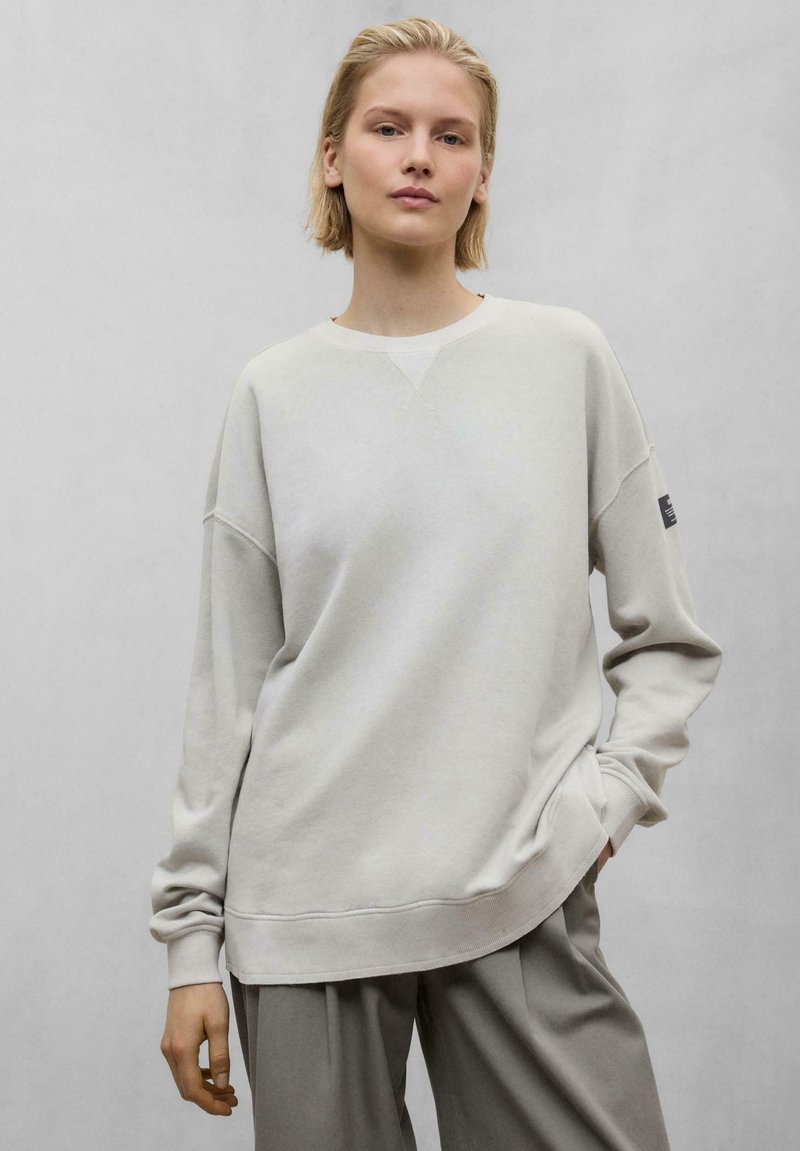 Sweatshirt gris clair avec un col rond, des épaules tombantes et des poignets côtelés. Texture douce ; coupe ample et décontractée. Design minimaliste sans motifs.