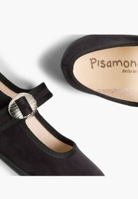 Ballerine in suede nero con punta tondeggiante, bordi elastici e una fibbia rotonda decorativa in argento sulla cinghia. L'interno è foderato in beige.