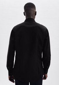 Zwarte langarmshirt met een gestructureerde kraag, ronde zoom en knoopmanchetten, voorzien van een gladde stoftextuur.