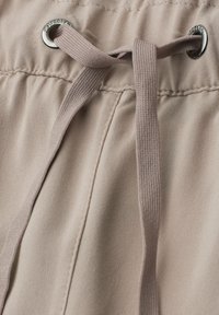 Tissu beige avec cordon tressé assorti passé à travers des œillets en métal sur la taille froncée d’un pantalon ou d’un short.