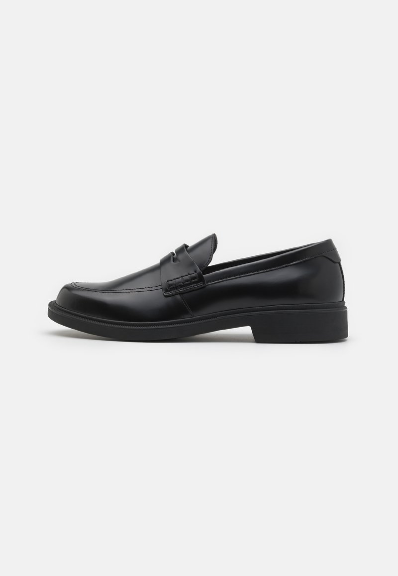 Melnas ādas loafers ar noapaļotu purngalu, izceltiem šuvumiem uz virsmas un plakanu gumijas zoli. Gluda tekstūra, klasiskā dizaina izskats.