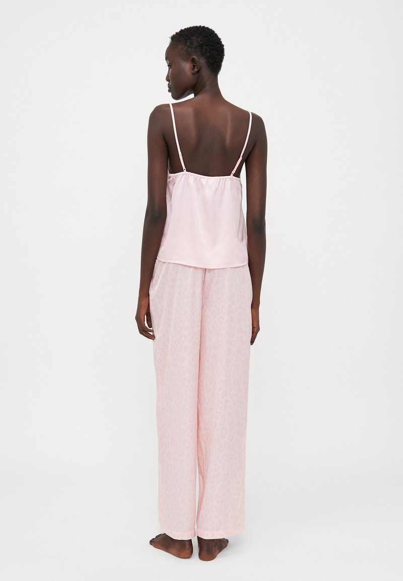 Camisole in satin rosa chiaro con spalline sottili e vita elasticizzata, abbinato a pantaloni rosa a gamba larga con un sottile motivo maculato.
