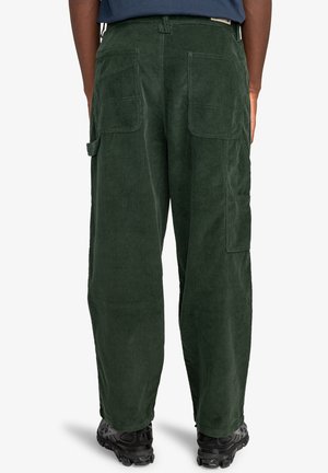 Green corduroy cargo pants with a relaxed fit, featuring two back pockets and a side pocket, paired with black textured footwear.
