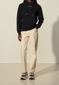 Felpa nera con cappuccio e lacci, pantaloni color crema e sneakers con motivo. Design semplice, materiale in cotone e colori a contrasto.