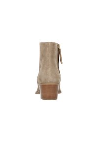 Bottes chelsea en suède beige avec un talon en bois et une tirée de zip visible à l'arrière, présentées de dos sur fond blanc.