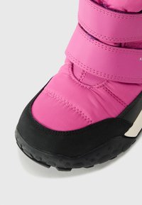 Botte imperméable rose avec semelle en caoutchouc noir, sangles Velcro et texture matelassée. Convient pour les temps froids et les activités en extérieur.
