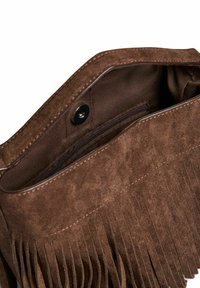 Brūna zamša rokassoma ar frizētā dizaina elementiem, kas aprīkota ar iekšējo zip kabatu un snap aizdari. Mīksta tekstūra un strukturēta forma.