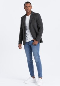 Grau karierter Blazer über einem weißen T-Shirt, kombiniert mit blauen Jeans und weißen Sneakers. Schmaler Schnitt, glatte Textur und taillierte Passform.
