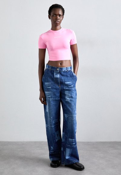 Růžové zkrácené tričko s logem, v kombinaci s volnými modrými džíny s tištěným vzorem novin. Černé boty dotvářejí celý outfit.