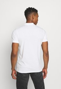 White short-sleeve polo shirt made of cotton, featuring a classic collar and a plain design with a slight stretch for comfort.