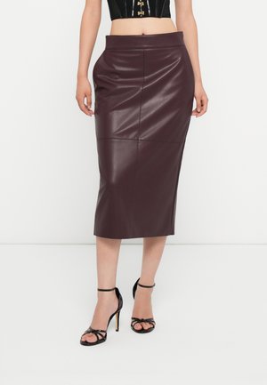 Saia lápis de imitação de couro cor bordeaux com silhueta ajustada, textura suave e detalhes em costura, combinada com sapatos de salto altos pretos com tiras.