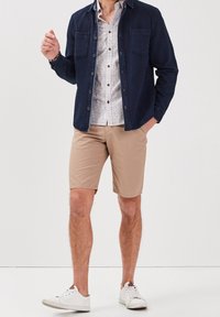 Navy button-up shirt with textured fabric over a white patterned shirt, paired with beige shorts and white sneakers.