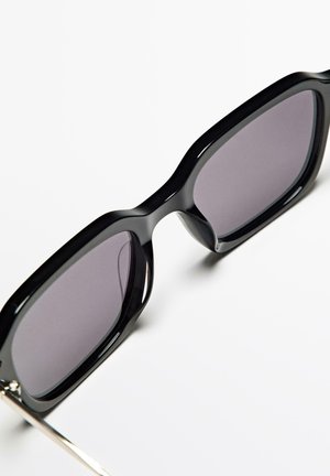 Black sunglasses with a thick, glossy frame and grey lenses. Features a sleek design with a silver metal accent on the temples.