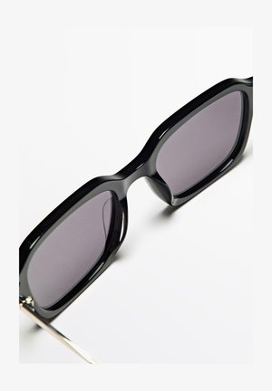 Schwarze Sonnenbrille mit einem dicken, glänzenden Rahmen und grauen Gläsern. Sie verfügt über ein elegantes Design mit einer silbernen Metallakzentuierung an den Bügeln.