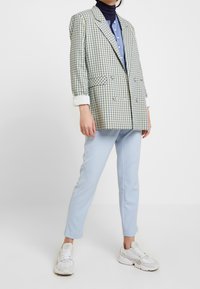 Sako má zelený a námořnicky modrý kostkovaný vzor, dvouřadý design a bílé manžety. Kombinováno s světle modrými kalhotami a bílými teniskami.