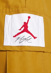 Žlutá látka s bílou nášivkou nesoucí červené logo Jordan a nápis „Flight“ pod ním, zdůrazňující sportovní design a detaily značky.