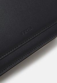 Czarny skórzany portfel o gładkiej teksturze, z dyskretnym wytłoczonym logo i kontrastowym szwem wzdłuż krawędzi.