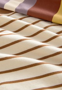 Tissu en coton à texture ondulée, présentant des rayures alternées crème et marron. La douceur visible et le mélange de couleurs rehaussent le design.