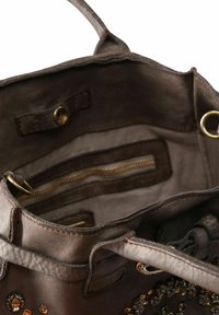 Interno di una borsa a tracolla in pelle marrone con una texture liscia, dotato di più tasche, un compartimento con zip e decorazioni a borchie.