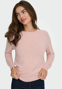 Maglione lavorato a maglia rosa chiaro con colletto rotondo, maniche lunghe e orlo leggermente curvo. Tessuto morbido, abbinato a jeans scuri.