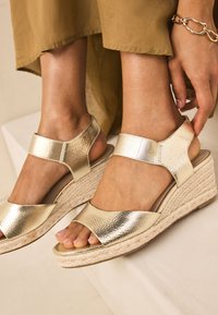 Sandales compensées métalliques dorées à bout ouvert, avec une partie supérieure texturée, des larges brides et une semelle plateforme en jute tressé.