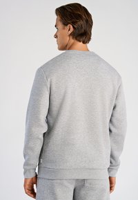 Felpa grigia dal taglio rilassato, con scollo tondo e polsini a coste. Tessuto morbido con finitura liscia e dettaglio del marchio sul lato.