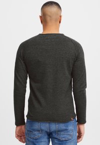 Chemise à manches longues gris foncé avec un design raglan, fabriquée en tissu texturé. Associée à un jean bleu avec un design arrière à deux poches.