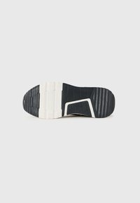Suola in gomma nero e bianco di una sneaker con modelli di grip testurizzati e scanalature curve, mostrata dal basso su uno sfondo uniforme.