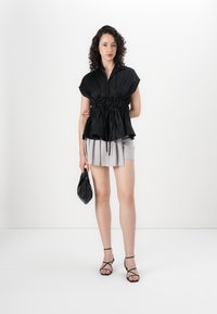 Sort kortærmet bluse med samlet talje, parret med en lys grå plisseret mini-sukker. Bærer en sort clutch og har strappy sorte sandaler på.