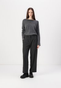 Grå stickad tröja med vid halsringning, i kombination med mörkt randiga byxor. Svarta platåskor fulländar outfiten.