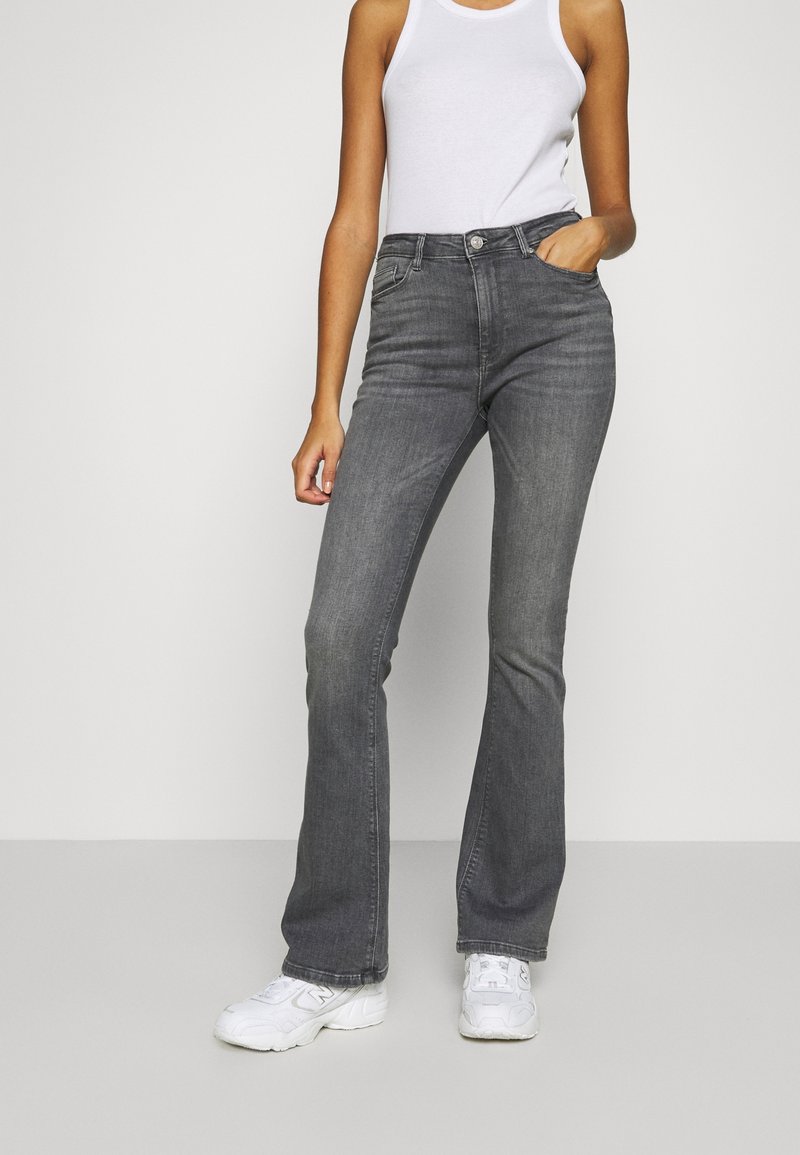 Grå utsvängda jeans med hög midja, fem fickor och knappstängning. Tyget uppvisar subtil textur, matchat med vita sneakers.