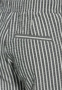 Šedo-bíle pruhovaná látka s texturovaným povrchem; obsahuje malou vodorovnou kapsu na pravé straně blízko pasu.