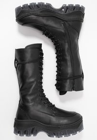 Bottes de combat en cuir noir avec tige haute, devant à lacets, fermeture éclair latérale et semelle en caoutchouc robuste et texturée présentant un motif de bande de roulement distinct.