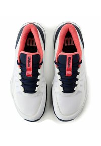 Zapatillas blancas con acentos azul marino, forro coral y suela negra en contraste. Presenta una lengüeta texturizada con el logotipo "Wilson" y cierre de cordones.