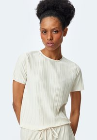 Top de color crema, de manga corta, con una textura acanalada, cuello redondo y un ajuste relajado. Combinado con pantalones de cintura ajustable a juego.