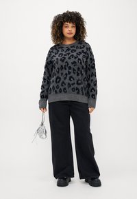 Sweater cinza com padrão de leopardo preto, textura aconchegante, punhos canelados, combinado com jeans pretos de perna larga e botas pretas robustas. Acento de bolsa transparente.