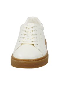 Bílé kožené tenisky s kulatou špičkou, šněrováním v přední části a hnědou gumovou podrážkou. Obsahují decentní logo na boku a strukturované akcenty na podrážce.