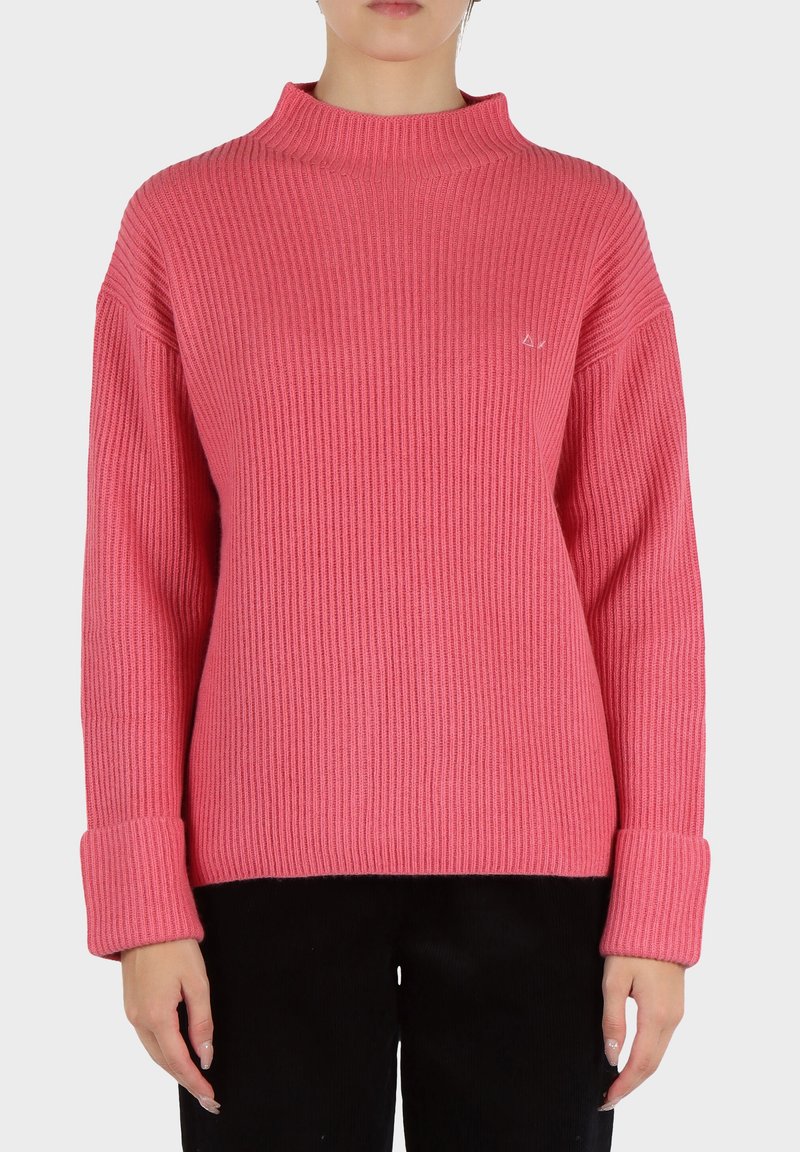 Pullover a coste in rosa brillante con collo alto, maniche ampie e dettagli ai polsini. Presenta un logo discreto sul petto.