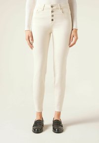 Jeans blancos de cintura alta con cierre de cinco botones, corte ajustado y dobladillo deshilachado; presentan bolsillos clásicos y un acabado suave y texturizado.