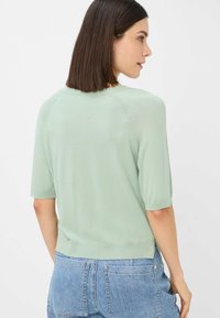 Top in maglia verde chiaro con maniche corte, scollatura tonda, orlo a coste e dettagli sulla cucitura posteriore, abbinato a jeans blu con vita alta.