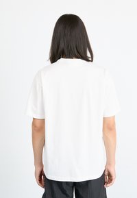 Hvit bomull t-skjorte med korte ermer, rund halslinning og et rent bakdesig. Stoffet har en glatt tekstur.