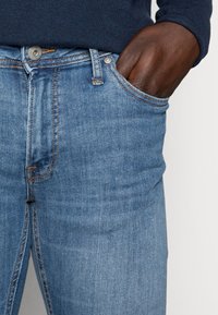 Jeans de denim azul claro con un corte clásico, que presentan un bolsillo frontal, costuras de contraste y un cierre de botón de metal.