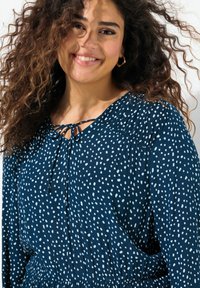 Tummansininen mekko valkoisilla pilkuilla, nauhakiinnike kaula-aukossa, ryppyiset olkapäät, pehmeä kangas ja joustava vyötärö.