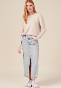 Maglione rosa chiaro con motivo a spina di pesce, abbinato a una gonna di jeans blu con spacco frontale. Scarpe da ginnastica bianche alte completano il look.