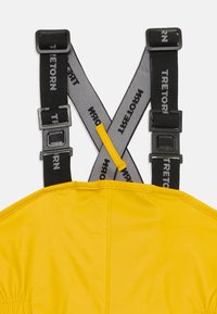 Busca uma roupa amarela à prova d'água com alças ajustáveis em preto e cinza, que apresenta uma marcação e uma textura suave e brilhante. O hardware inclui clipes de plástico.