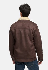 Braune Wildlederjacke mit einem cremefarbenen Kunstfellkragen, im entspannten Schnitt und mit klaren Linien, kombiniert mit blauen Jeans.