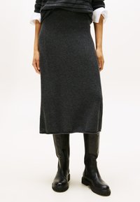 Grijze gebreide midi-rok van zachte wol, met een rechte silhouet en een elastische tailleband, gecombineerd met zwarte laarzen tot de knie.