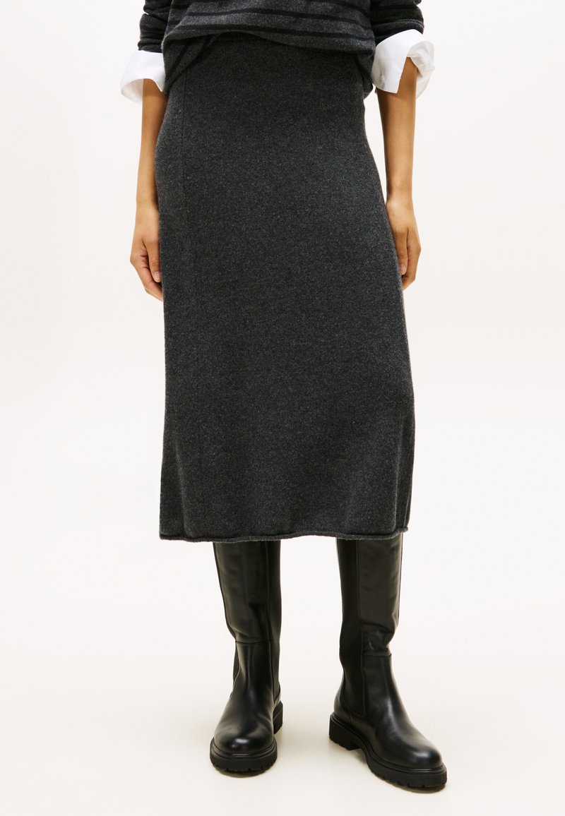 Grijze gebreide midi-rok van zachte wol, met een rechte silhouet en een elastische tailleband, gecombineerd met zwarte laarzen tot de knie.