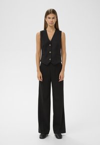 Juodas pritaikytas liemenė su V formos iškirpte ir penkiais mygtukais, derinama su laisvomis juodomis kelnėmis. Lygus audinys su oficialiu dizainu.