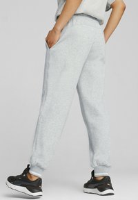 Pantalones de chándal gris claro con cintura y puños elásticos, que cuentan con bolsillos laterales y una textura suave, combinados con zapatos deportivos negros.